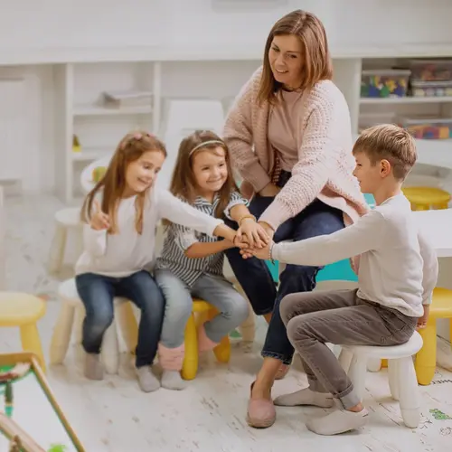 Eine Erzieherin mit drei Kindern, die ihre Hände aufeinander legen.